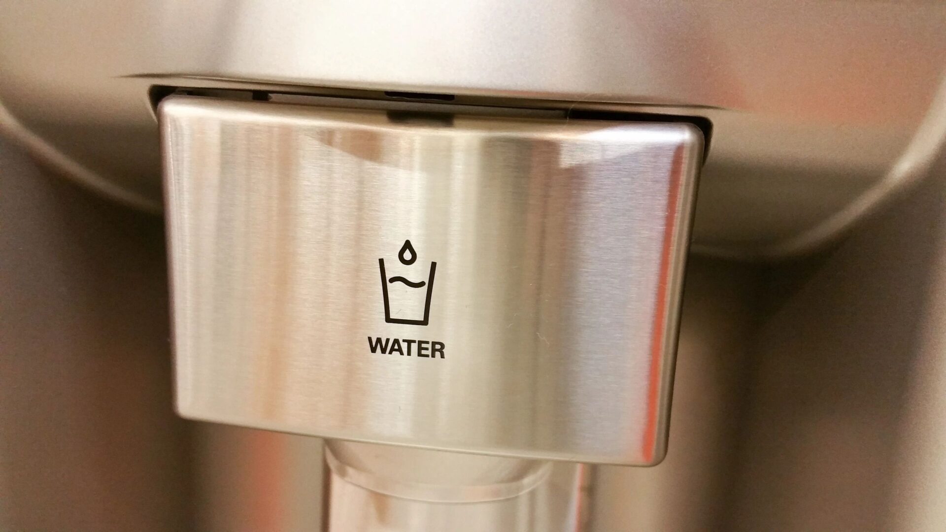 A close up of the water dispenser on a stainless steel wall.